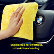 Hand using a yellow microfiber cloth to clean a BMW car interior.