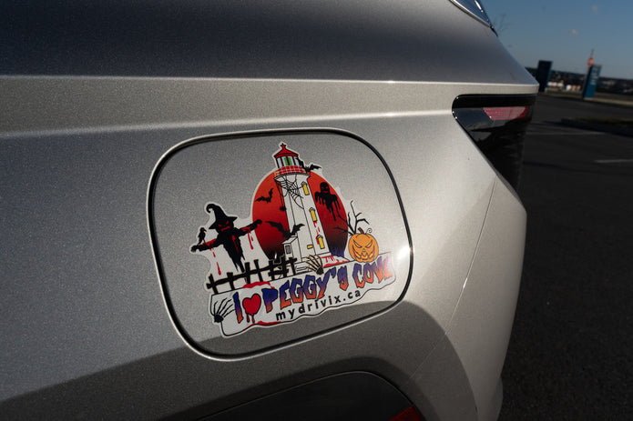 Halloween-themed sticker on a car's fuel cap with a lighthouse and pumpkin design.