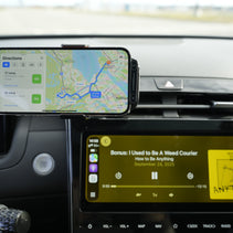 Phone mounted on a car dashboard displaying navigation and music app.