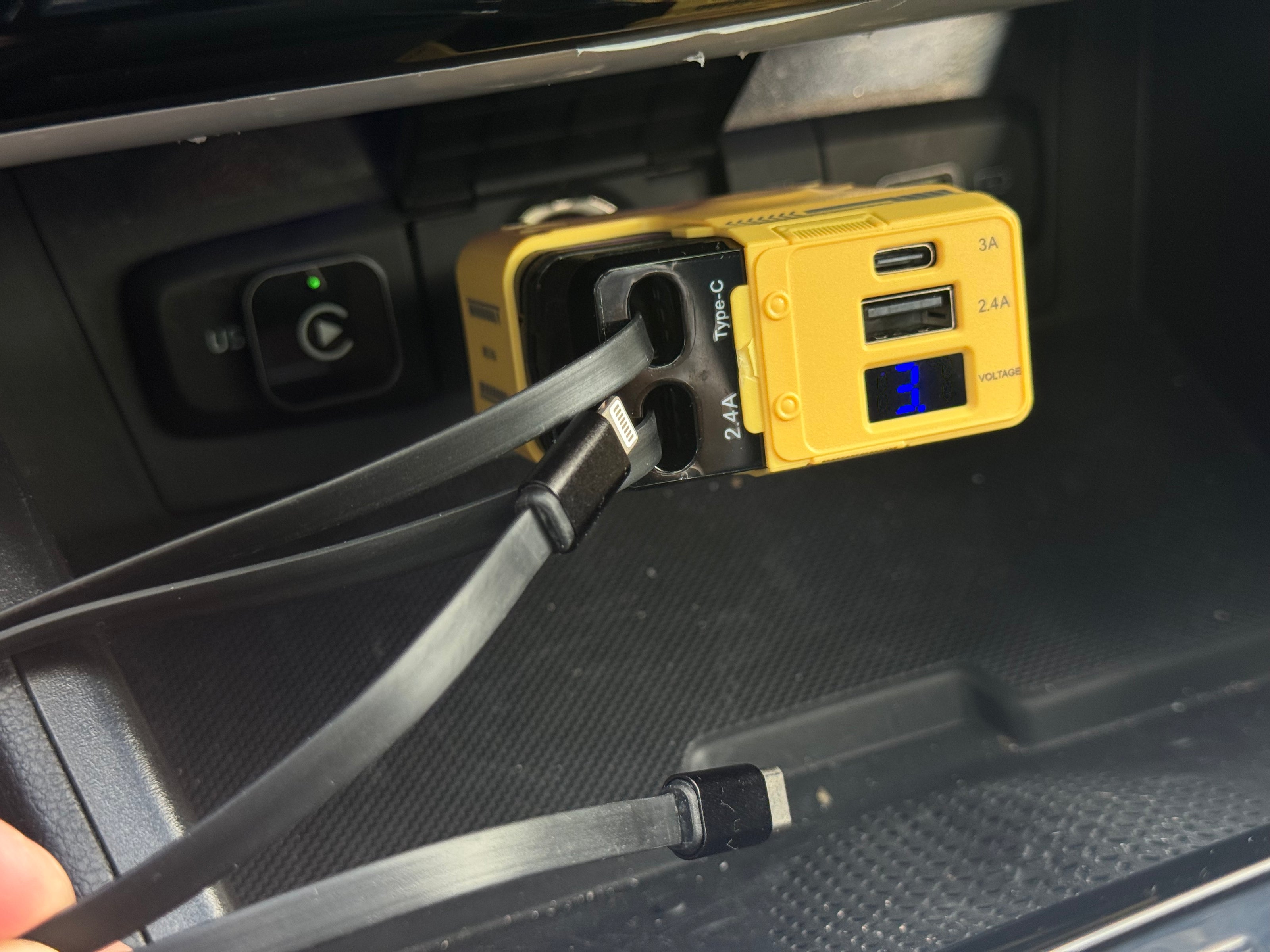 Yellow power adapter with USB ports and cable plugged into a car's USB port.