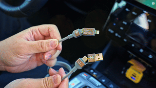 Hands holding a braided multi-device car charging cable, showing USB and phone connectors inside a vehicle.