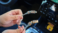 Hands holding a braided multi-device car charging cable, showing USB and phone connectors inside a vehicle.