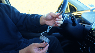 Person holding a flexible coiled charging cable inside a car near the steering wheel.