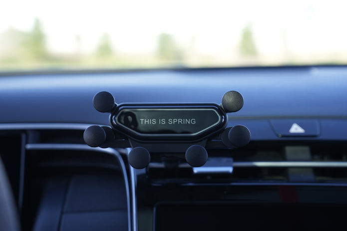 Phone holder on a car dashboard with 'This is Spring' text