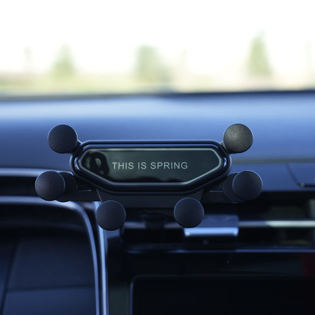Phone holder on a car dashboard with 'This is Spring' text