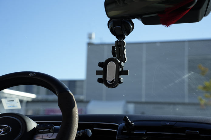 Phone holder attached to a car's rearview mirror with a blurred outdoor background