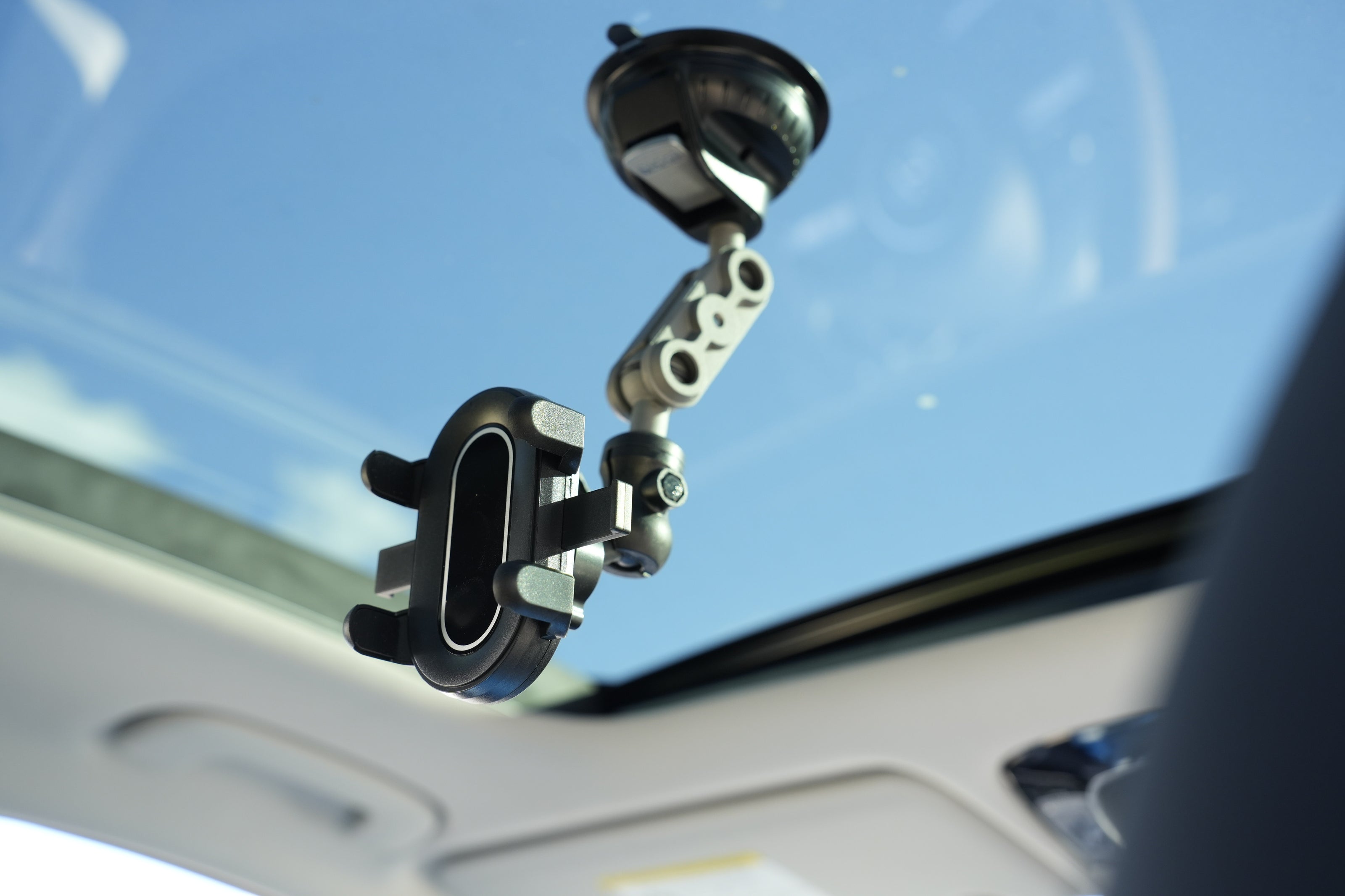 Car phone mount attached to a car's sun visor with a clear blue sky background.