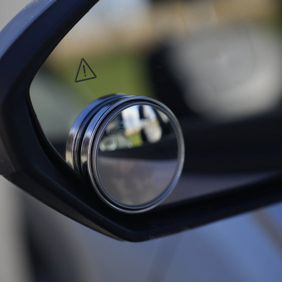 Close-up of a car side mirror with a warning triangle on a blurred background