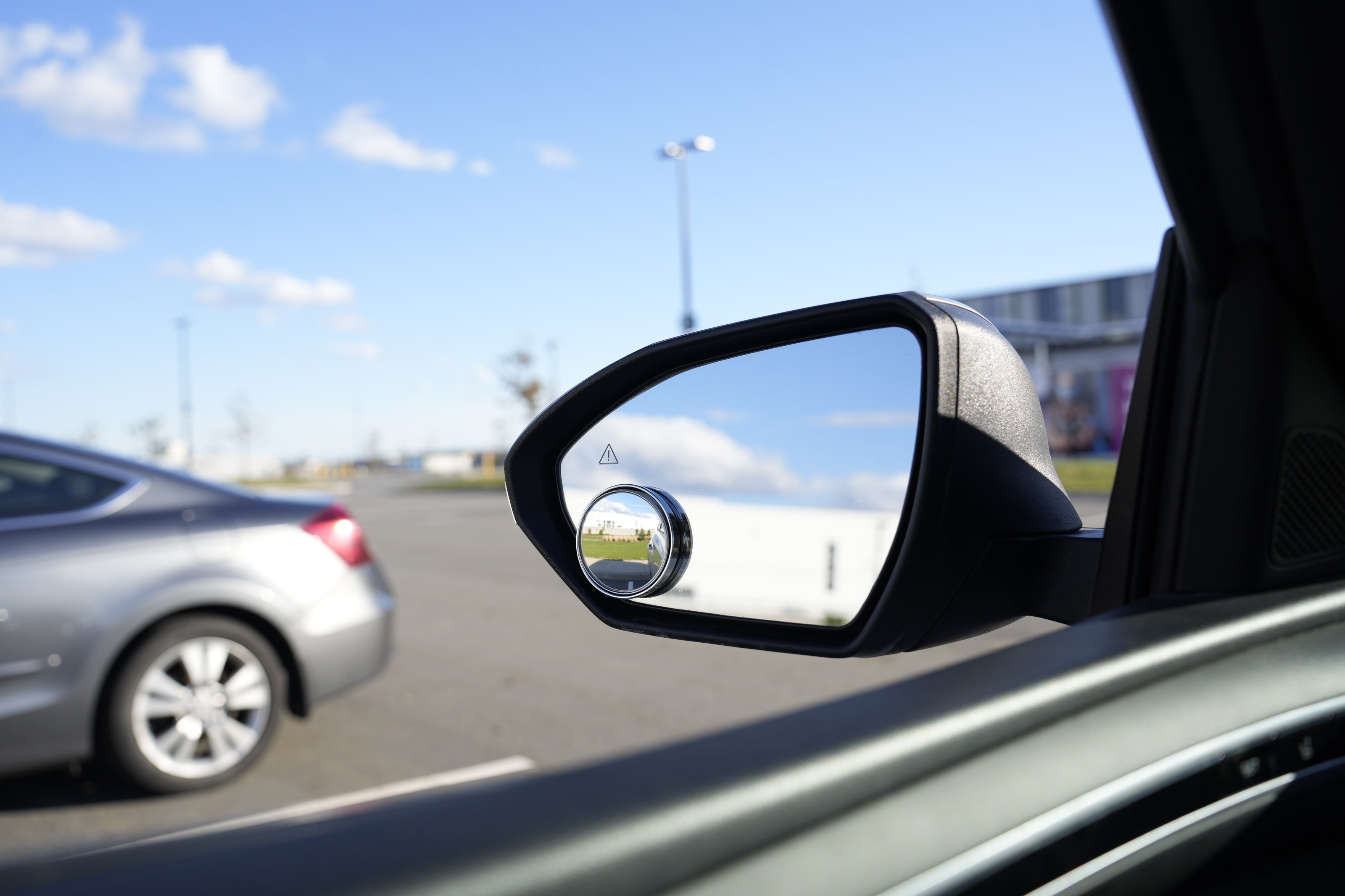 Car side mirror reflecting a road scene with another car in the distance.