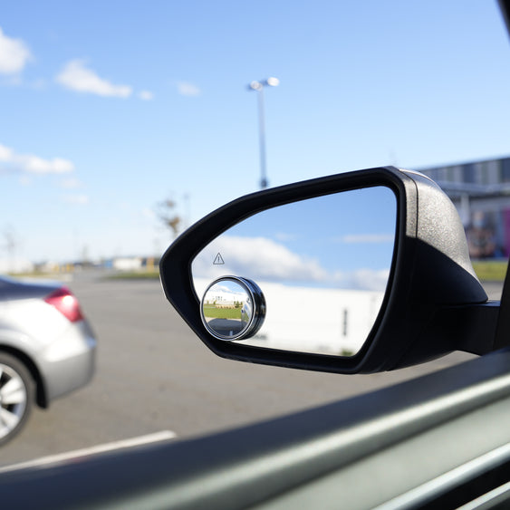 Car side mirror reflecting a road scene with another car in the distance.